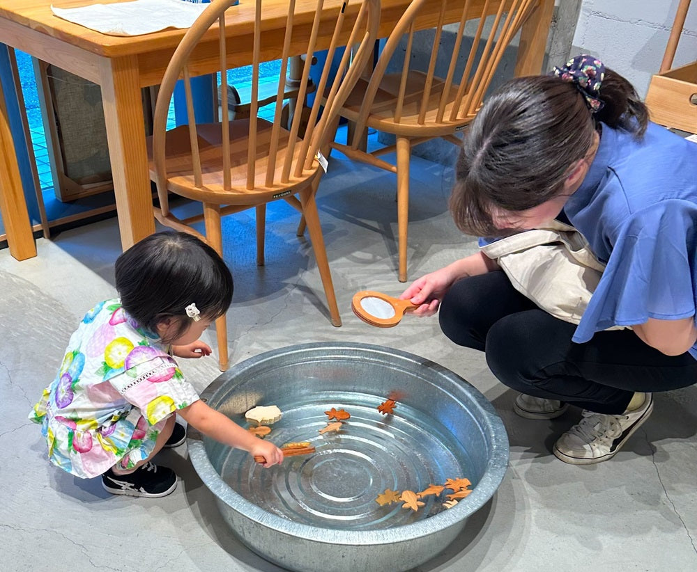 なかよしライブラリー吉祥寺店　木の金魚すくいで遊ぶ女の子とお母さん